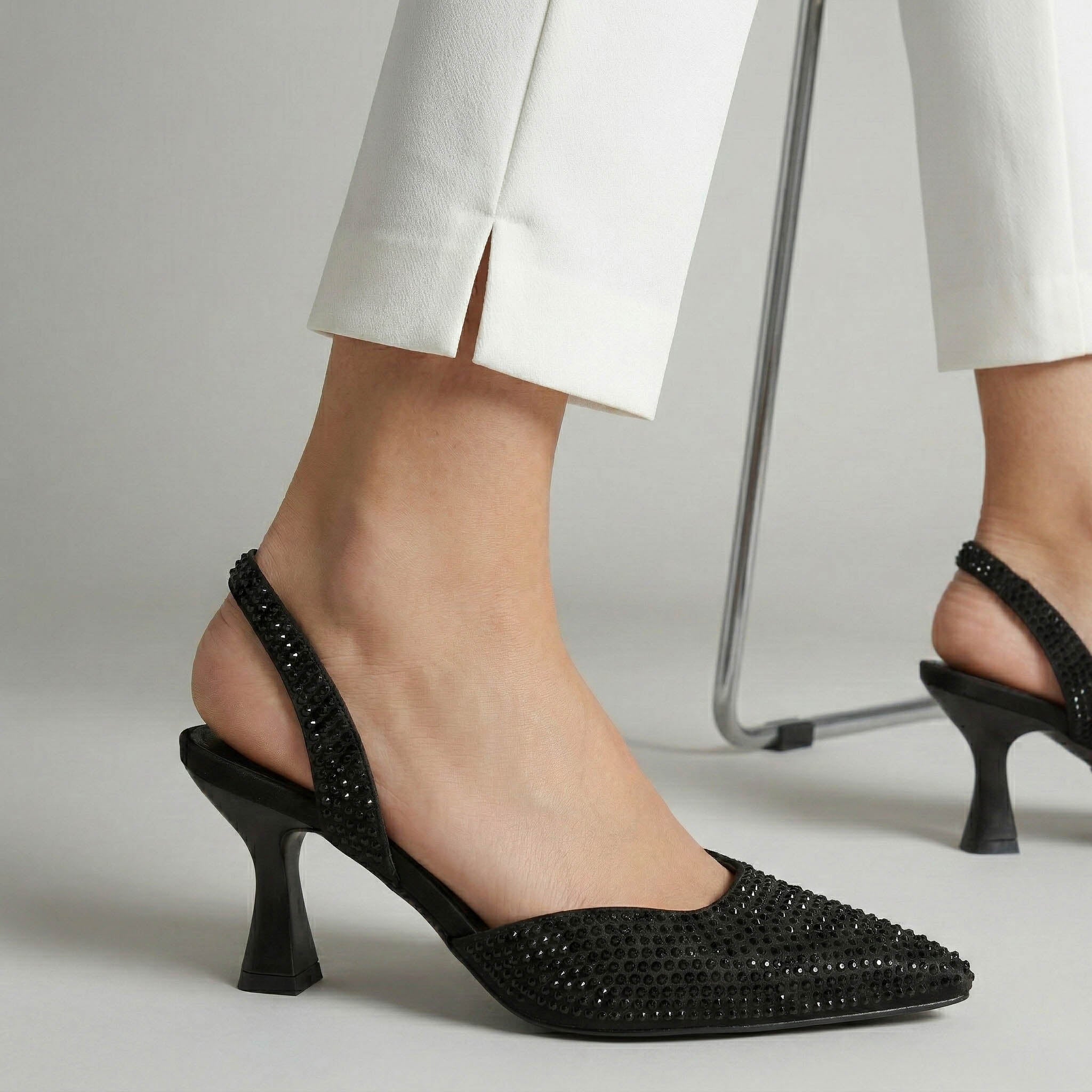 Black high-heeled shoes worn with white pants on a neutral background
