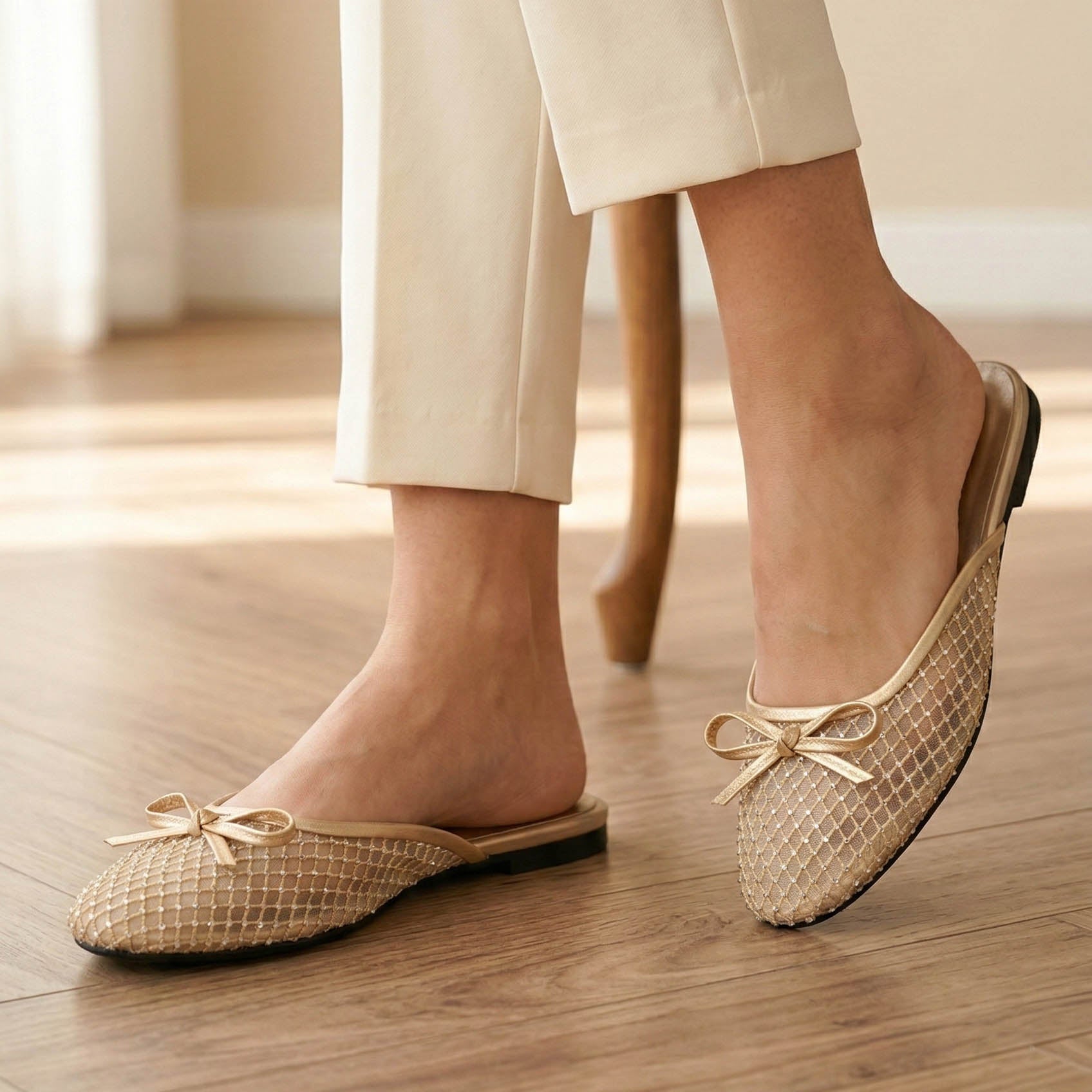 Beige woven flats with bow details worn by a person on a wooden floor.