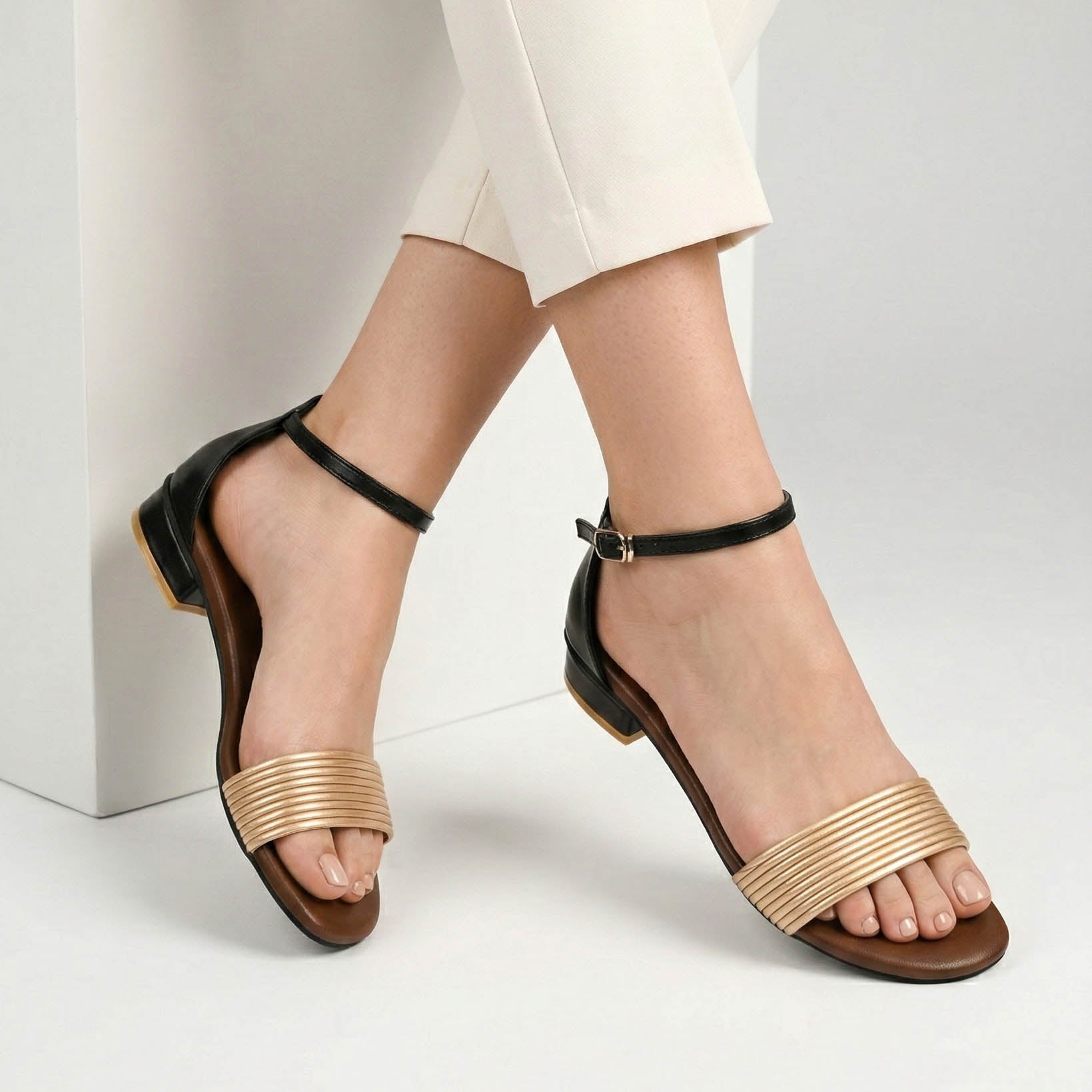Black sandals with gold straps worn by a person on a light gray background