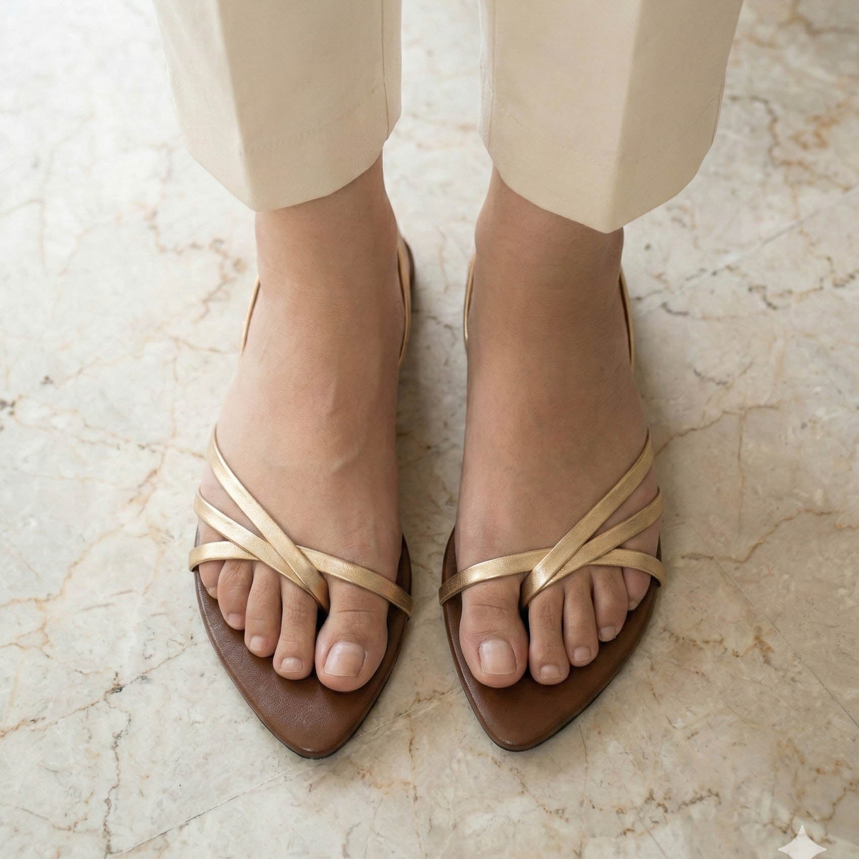 Brown sandals with gold straps worn on a marble floor