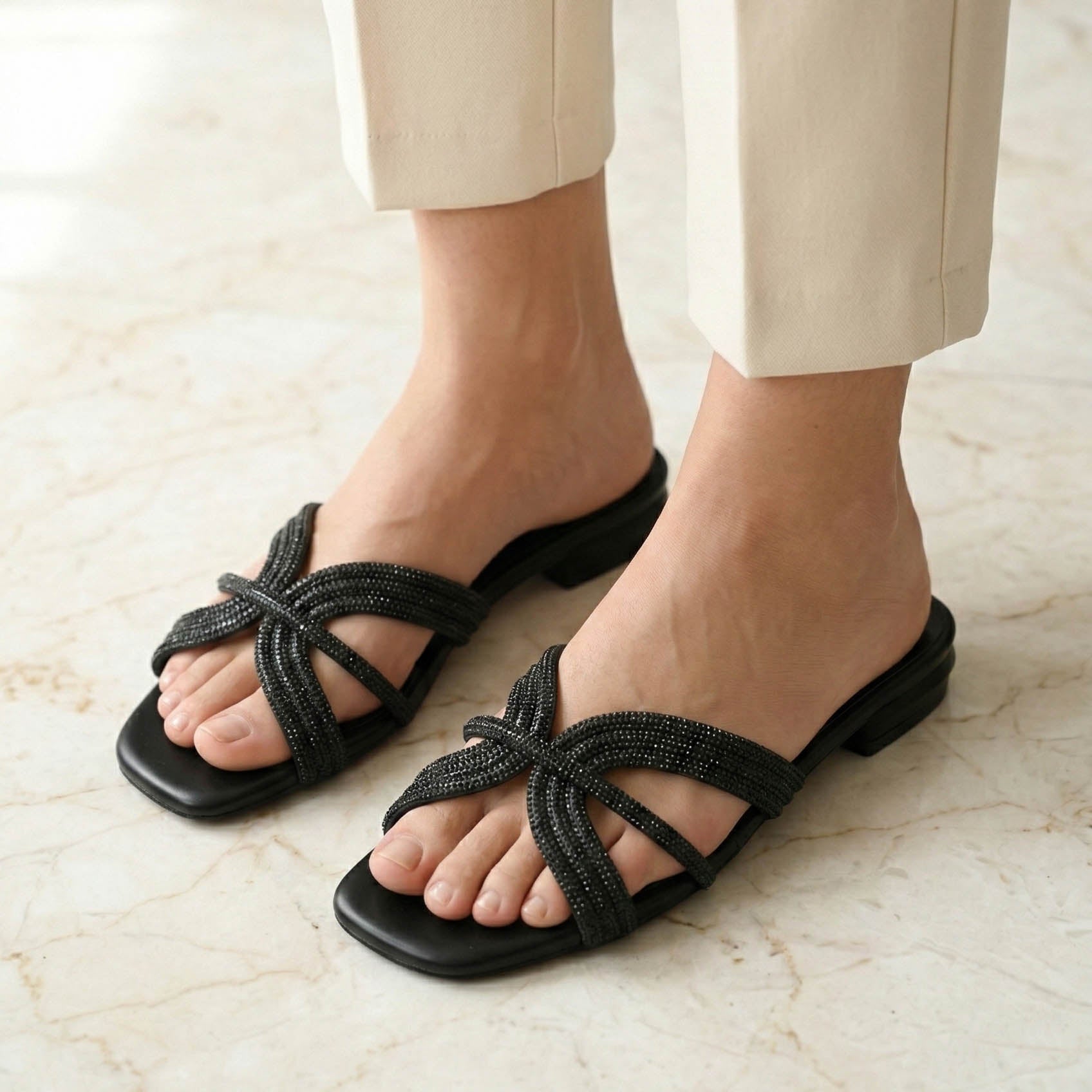 Black sandals worn with beige pants on a light marble floor