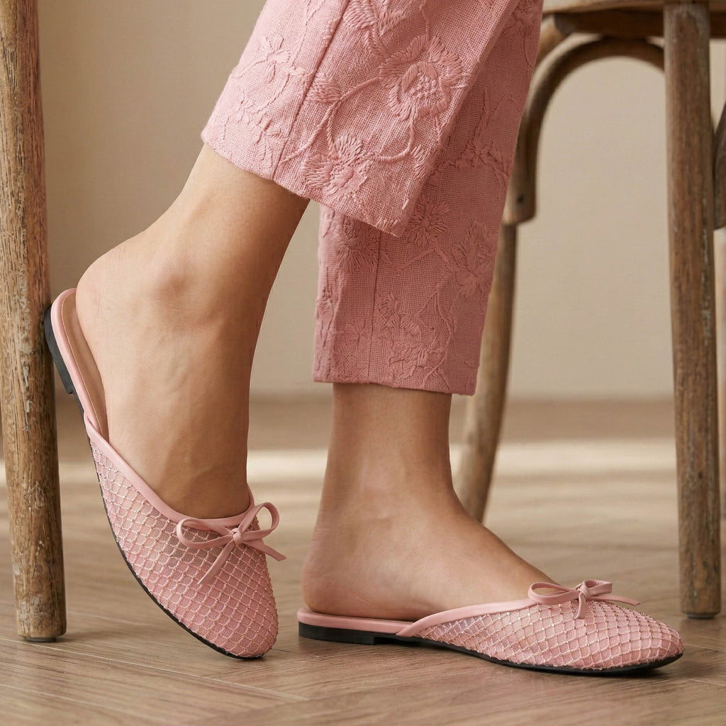 Pink slippers with a bow worn by a person sitting on a wooden chair.
