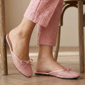 Pink slippers with a bow worn by a person sitting on a wooden chair.