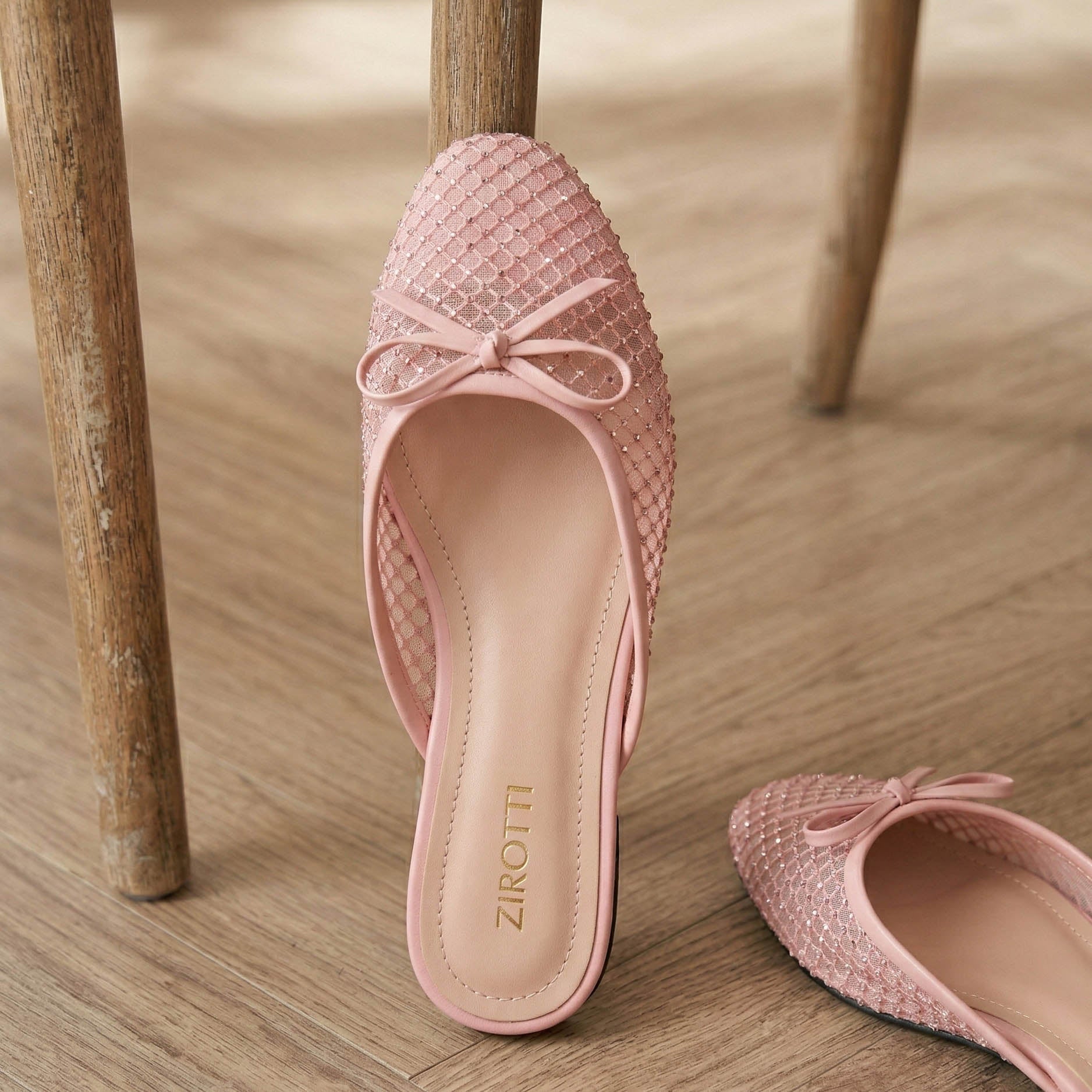 Pink woven shoes with a bow on a wooden floor, featuring the brand 'Zirotti'.