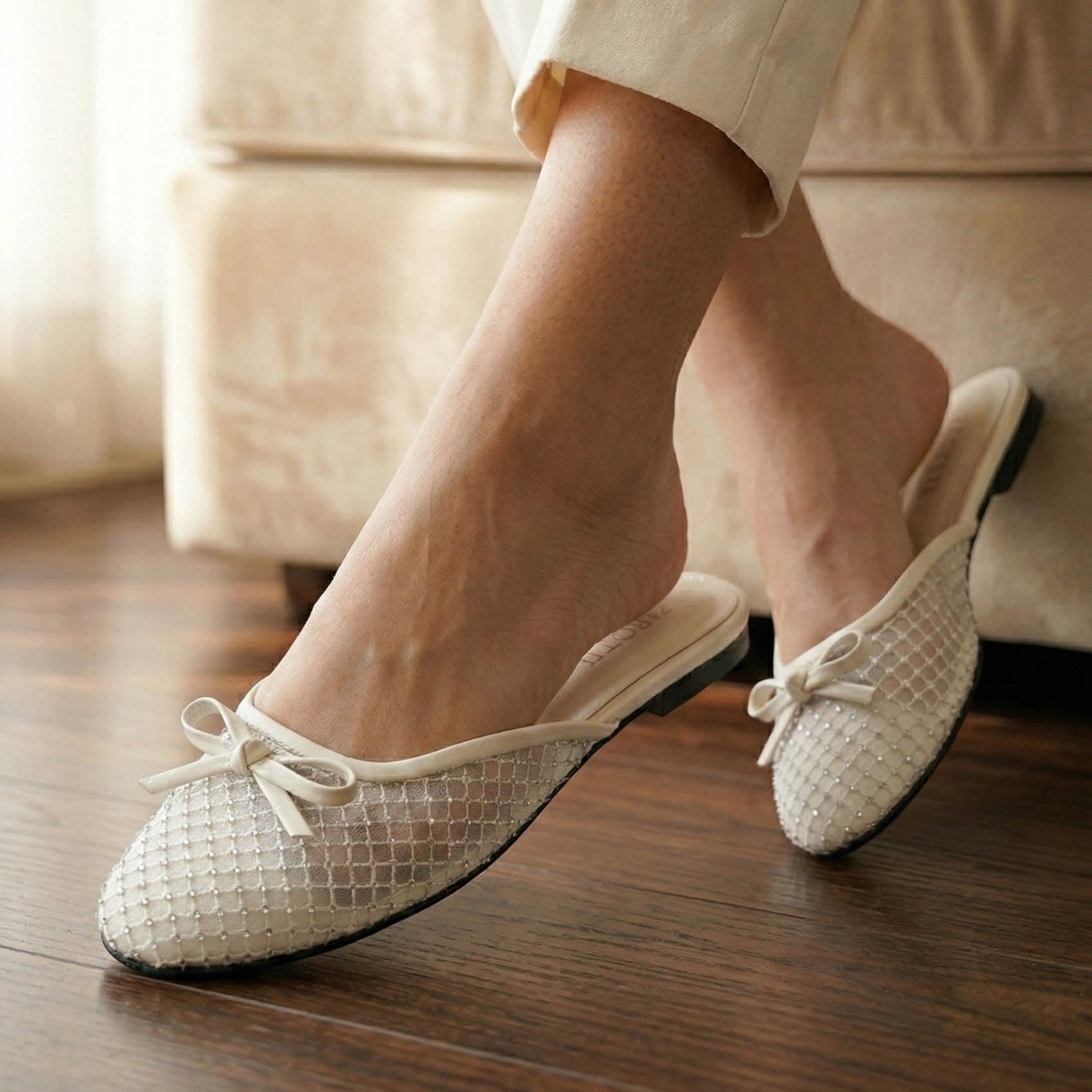 White woven shoes with black soles worn by a person sitting on a beige couch.