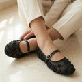 Black embellished shoes worn with beige pants on a light wooden floor.