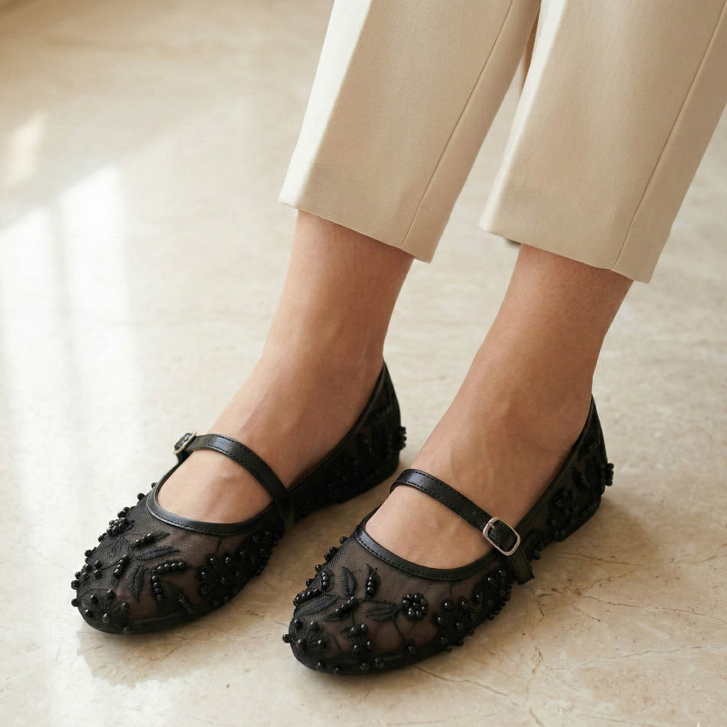 Black embellished shoes worn with beige pants on a light background